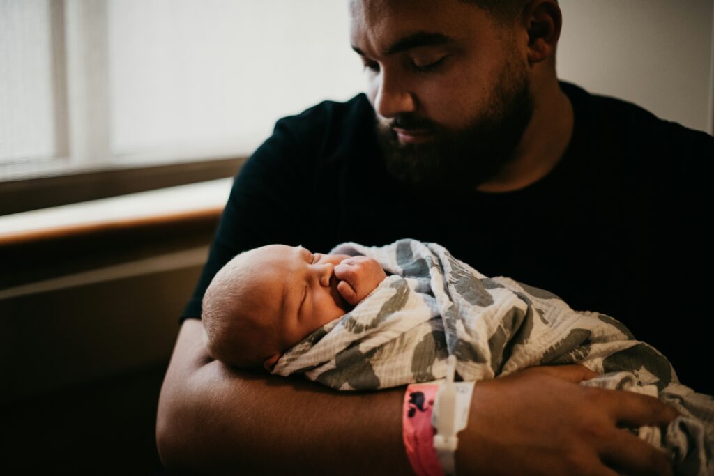 A father holding his newborn infant during paid leave.